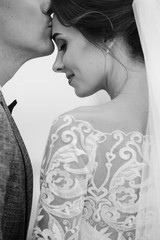 Black and white wedding photo. Groom kisses bride on forehead. Stylish newlyweds