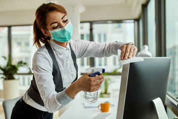 Wall Mural - Businesswoman with face mask cleaning her computer in the office.