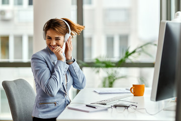 Wall Mural - Young businesswoman having fun while listening music over headphones in the office.