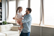 © fizkes - Loving dad holds on hands small daughter she wears crown imagines herself like princess, people dancing in living room, enjoy holiday life event birthday party. Happy fatherhood, family bonds concept