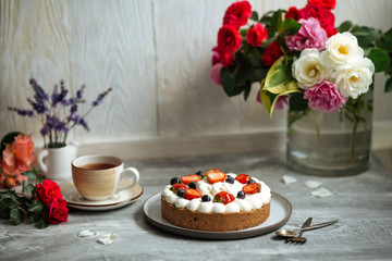 Wall Mural - Side view on appetizing sweet cake with white cream and decorated with berries on the grey background with a cup of tea, horizontal
