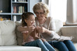 © fizkes - Senior grandmother teaches little granddaughter to knit seated on couch, multi generational people loving family holding needles and yarn, hobby and fun, activity to improve fine motor skills concept