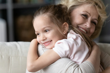 Wall Mural - Aged grandmother caresses beloved granddaughter hugs her strong snuggles enjoy time together at home close up image. Life value, deep connection between different generations relatives people concept