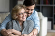© fizkes - Happy senior mother spend time with grown up son, relatives people hugging at home, adult attentive millennial grateful child wrapped in a plaid or warm sweater loving mommy caring about her comfort