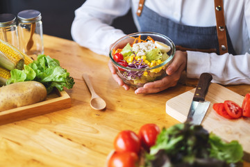 Closeup image of a female chef cooking and holding a bowl of fresh mixed vegetables salad in kitchen