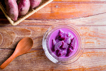 Top view purple sweet potato with coconut milk in transparent bowl and spoon on wooden table. Delicious Thai dessert.