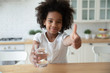 Portrait of happy small biracial girl hold water glass show thumb up recommend healthy lifestyle, smiling little African American child give recommendation for clean mineral aqua for body refreshment