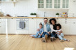 © fizkes - Portrait of happy multiracial young family with little kids sit on warm floor in design modern kitchen, smiling multiethnic parents with small biracial daughters relax in new renovated home together