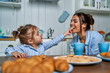 © Тарас Нагирняк - Little daughter feeds her mother with sweet cookies. Family having fun in the kitchen during breakfast at home