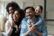 © fizkes - Happy biracial girls hug piggyback smiling young multiracial parents enjoy weekend at home together, overjoyed small multiethnic daughters embrace play with loving mom and dad on quarantine