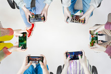 Hands Of People Playing Multiplayer Online Games With Friends On Phones While Sitting In A Bright Room. Phone Screens Are Isolated In Color. In The Center Is An Empty Place For Inscriptions.