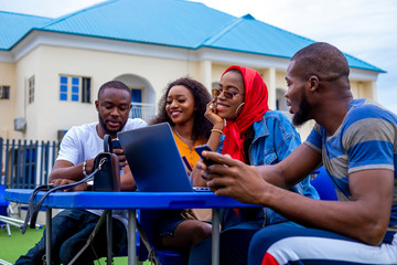 young black friends sitting out, having fun and using a laptop