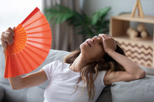 Overheated Woman Sitting On Couch, Waving Orange Paper Fan Close Up, Girl Feeling Unwell, Suffering From Heating At Home, Feeling Discomfort, Hot Summer Weather Or Fever, Sitting On Couch Alone