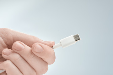 Wall Mural - Fingers holding white type-c cable connector on a gray background.