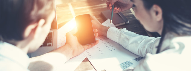 Fototapete - Group of business people working together. Loft office and smart casual dress code. Researching new product strategy. Electronic devices and paperwork on the table. Intentional sun glare effect. Wide 