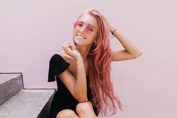 Wall Mural - Amazing european woman chilling on stairs after walk around town and smiling to camera. Pink-haired inspired girl in dress posing on the steps.