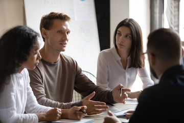 Wall Mural - Diverse young businesspeople brainstorm consider financial business ideas at team briefing in office, concentrated multicultural colleagues talk discuss company plan share thoughts at meeting