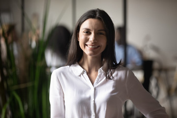 Happy caucasian young female leader posing at workplace look at camera smiling, close up headshot portrait of positive woman employee make picture in office, leadership, employment concept