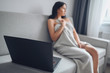 © Алина Троева - Beautiful woman using laptop, making a video call, working online at home, writing email, watching social network or movie, sitting in comfortable grey couch under warm blanket at home. Self isolation