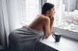 © Алина Троева - Beautiful bored slender brunette woman sitting next to window windowsill under warm grey blanket at home. Self isolation quarantine during Corona virus pandemic. COVID19 stay home save lives concept