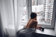© Алина Троева - Beautiful bored slender brunette woman sitting next to window windowsill under warm grey blanket at home. Self isolation quarantine during Corona virus pandemic. COVID19 stay home save lives concept