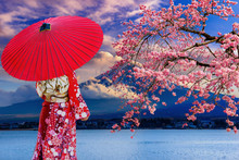 Asian Women Wear Japanese Kimonos. Holding A Red Umbrella At Mount Fuji And Cherry Blossoms At Lake Kawaguchiko In Japan.