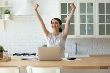 Young attractive woman exulting using calculator and laptop for calculating finance rates looking at screen. Successful girl happy hands up accounting with check credit analytic for mortgage payment.