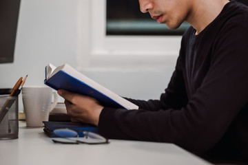 Young man reading book at work desk late at night, Knowledge and learning concept.