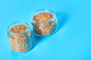 Two full glass jars of grain of buckwheat on blue table in kitchen. Agricultural concept