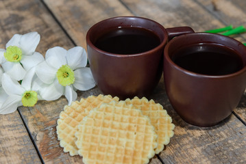 Two cups with coffee on the table. Breakfast for two. A bouquet of daffodils and coffee in bed.