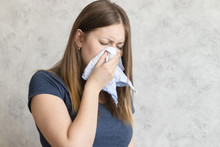 Sick Woman With Handkerchief Sitting At Home With Flue, Virus, Cold, Seasonal Allergy Symptom. Young Woman Blows Her Nose Or Sneezing In A Blue Cloth Handkerchief