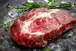 Raw fresh rib eye beef steak on ice with herbs and rosemary