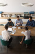 © fizkes - Vertical top view multi-ethnic businesspeople sitting at desk gathered in modern board room discussing planning solve common problems. Concept of teamwork, partnership and brainstorm image from above