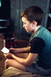 Portrait of a pensive unhappy boy with a smartphone in the room. A teenager with a mobile phone looks at a white screen. View messages, play, learn online, video conference. Horizontal image