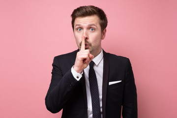 Young caucasian man making silence gesture asking to keep secret.