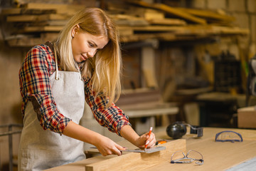 beautiful caucasian carpenter woman making marks on wooden piece before drilling, industry and handicraft concept