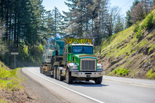 Green Powerful Big Rig Semi Truck With Oversize Load Yellow Sign On The Roof Transporting Crawler On The Step Down Semi Trailer Running Uphill On The Winding Mountain Road