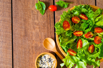 Fresh green vegetable salad. above of cherry tomato, onion, spinach and lettuce in wooden bowl with spoon, salad sesame dressing. Home made, Diet food for tasty and healthy meal. Top view, copy space.