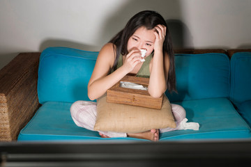 Wall Mural - young cute and emotional Asian Chinese woman watching korean drama show on TV sitting at home living room couch crying wiping tears with tissue paper