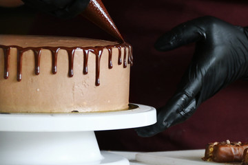 Wall Mural - liquid chocolate on cake. A confectioner squeezes liquid chocolate from a pastry bag on to a cream biscuit cake with background