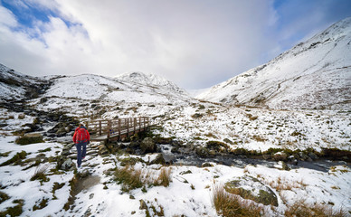 Wall Mural - A hiker crossing Glenridding Beck over a wooden bridge on route to a snow covered Catstye Cam and Helvellyn in the English Lake District.