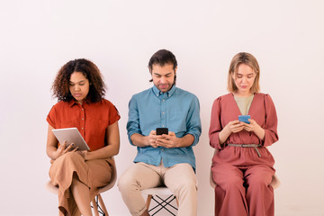 Wall Mural - Addicted young multi-ethnic people sitting in line and focusing on social media while using gadgets