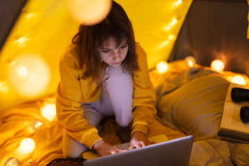 Wall Mural - little 11 year old girl using laptop under her home-made tent inside the living room.