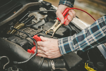 Hands of car mechanic using car battery jumper cable