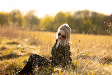 Wall Mural - Blonde girl is sitting at countryside in sunset time