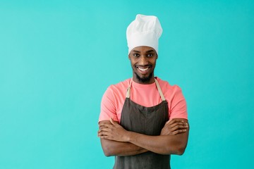 Canvas Print - Portrait of a smiling young male chef with arms crossed, against blue studio background