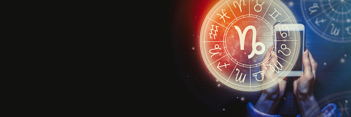 Wall Mural - female hands are holding a phone and an astrological circle with the zodiac sign capricorn on a back
