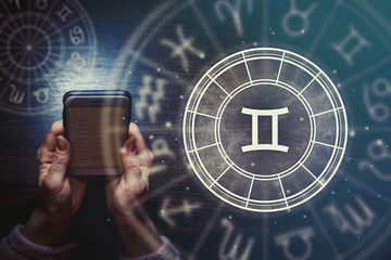 Wall Mural - female hands are holding a phone and an astrological circle with the zodiac sign gemini against a st