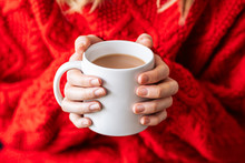 Close-up Of Young Woman With Red Cotton Sweater Holding A Hot White Coffee Mug With Her Hands. Winter Time.