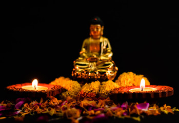 two amazing clay lamp glowing on rose petals against blurred buddha in the background. faith and buddhism concept.